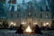 Diamond Painting mit dunkel gekleideten Gestalten an einem Feuer vor einer beleuchteten gotischen Villa.