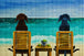 Diamond Painting von zwei Hunden, die in gelben Stühlen an einem Strand sitzen und auf das türkisfarbene Meer schauen. Mockup.