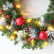 Detailansicht des Weihnachtskranzes mit Tannengrün, roten Kugeln, Tannenzapfen und warmweißen LED-Lichtern