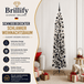 Schneebedeckter schmaler künstlicher Weihnachtsbaum mit schwarzen Kugeln als festliche Dekoration im Wohnzimmer