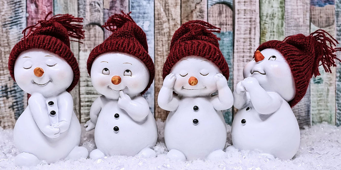 Diamond Painting von vier kleinen Schneemann-Figuren mit roten Mützen vor einer bunten Holzwand im Schnee. 
