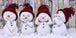 Diamond Painting von vier kleinen Schneemann-Figuren mit roten Mützen vor einer bunten Holzwand im Schnee. 
