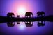 Diamond Painting von Elefanten-Silhouetten vor einem lila Sonnenuntergang mit Spiegelung im Wasser.