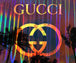 Diamond Painting mit Gucci-Schriftzug, Doppel-G-Logo, Federn und bunten Lichtstreifen auf dunklem Hintergrund.