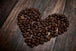 Diamond Painting mit Kaffeebohnen in Herzform auf dunklem Holztisch.