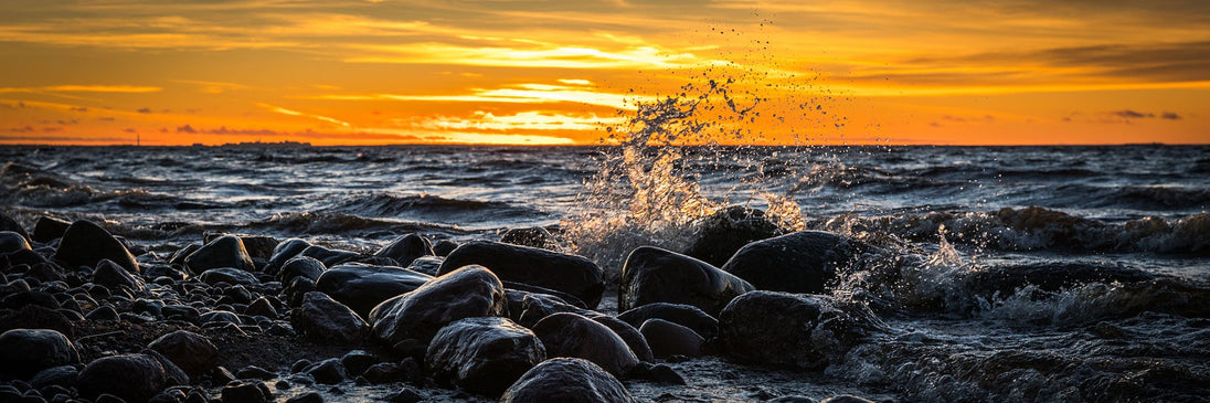 Diamond Painting einer vertikalen Küstenszene mit großen Felsen im Meer bei goldenem Abendlicht. 

