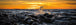 Diamond Painting einer vertikalen Küstenszene mit großen Felsen im Meer bei goldenem Abendlicht. 
