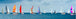 Diamond Painting einer Regatta mit vielen bunten Segelschiffen auf blauem Wasser unter bewölktem Himmel.
